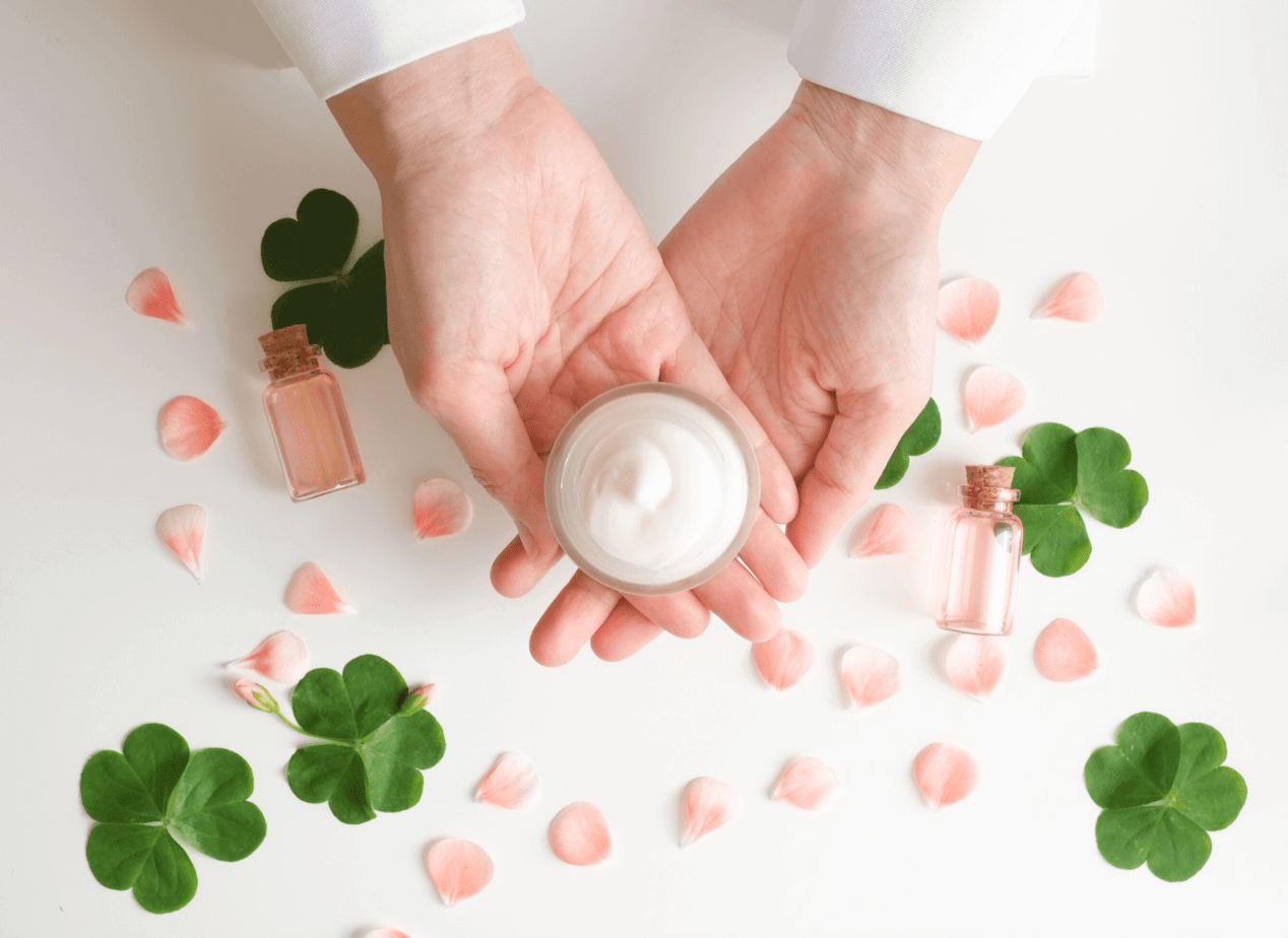 Two hands surrounded by leaves hold a clean beauty product